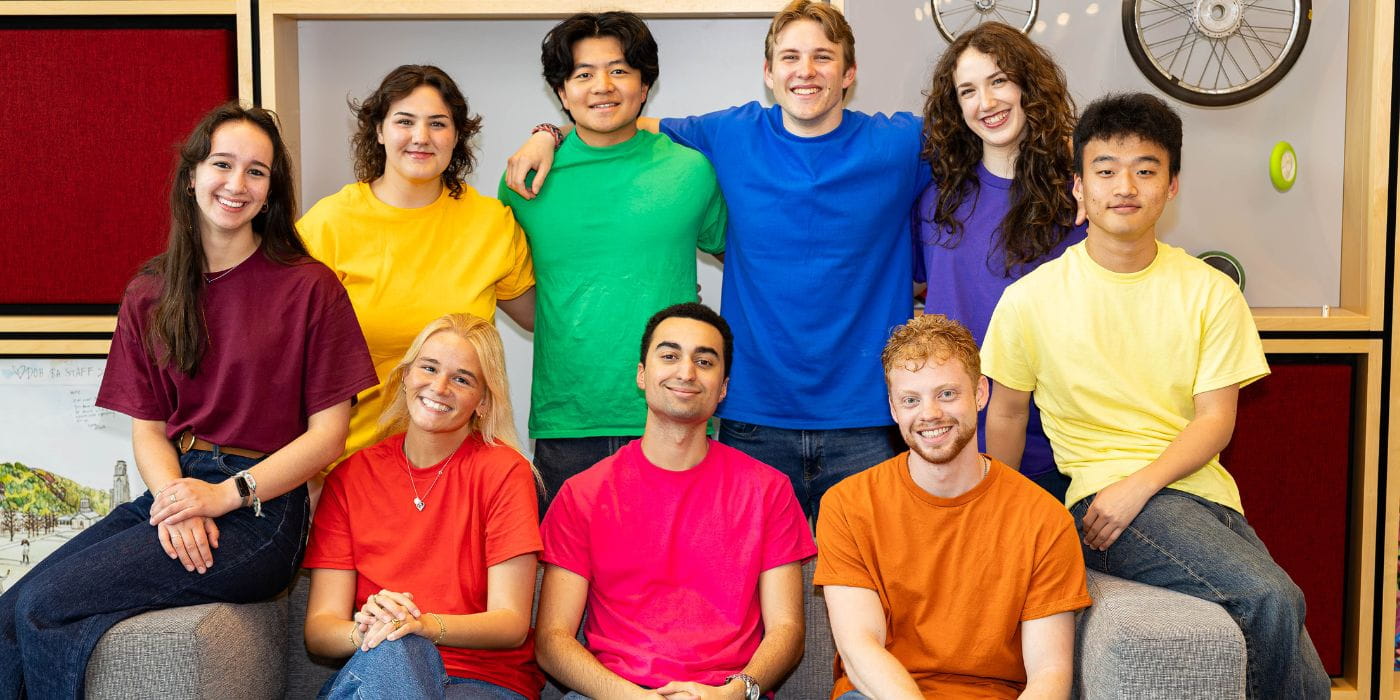 9 head orientation counselors stand together in shirts matching their housing community colors