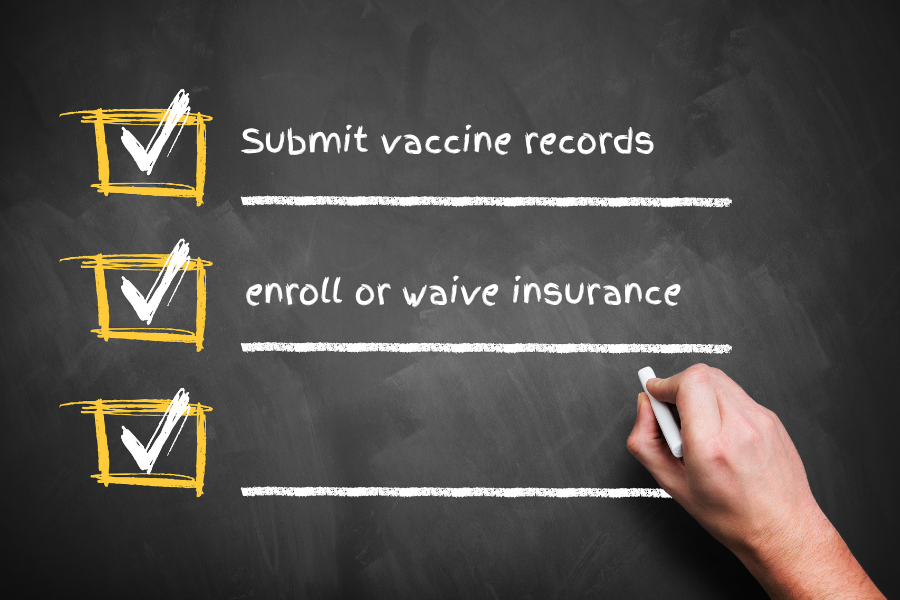 a checklist is being written on a chalkboard by a hand, the checklist says "submit vaccine records" and  "enroll or waive insurance"