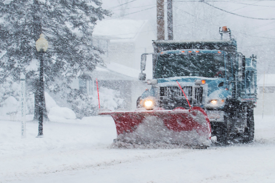 a snow plow truck plows a snowy street