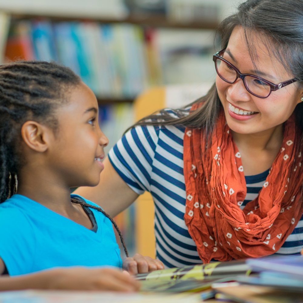 Student sits with teacher at a table.