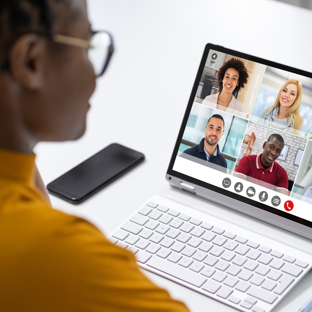 A woman sits in front of her laptop. Her screen is visible and shows a grid of the other people in the meeting.