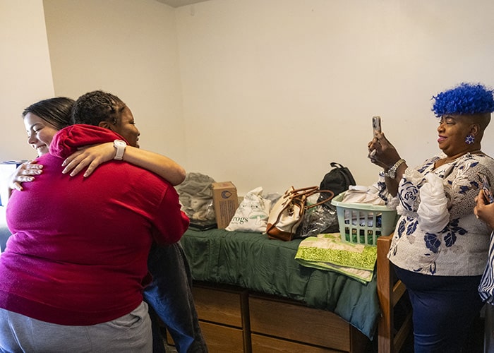 two new roommates hug while a mom takes a photo