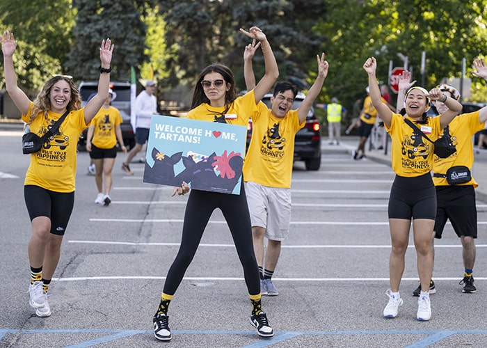 students in yellow t-shirts do a dance with a welcome home tartans sign