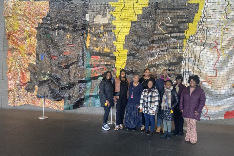 Sankofa members posing as a group in front of a large, colorful tapestry the Carnegie Museum of Art