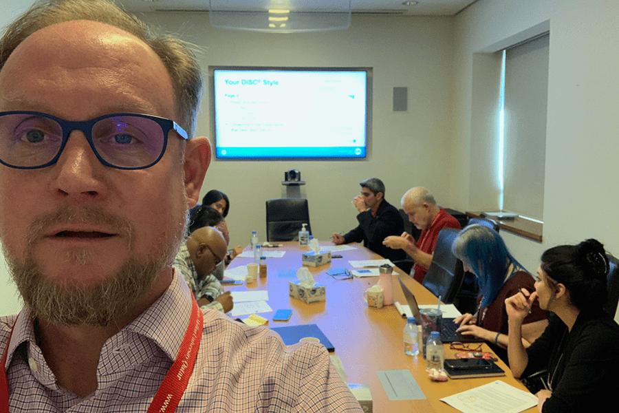 Selfie of Adam Marks leading a DiSC session with participants seated around conference table in the background