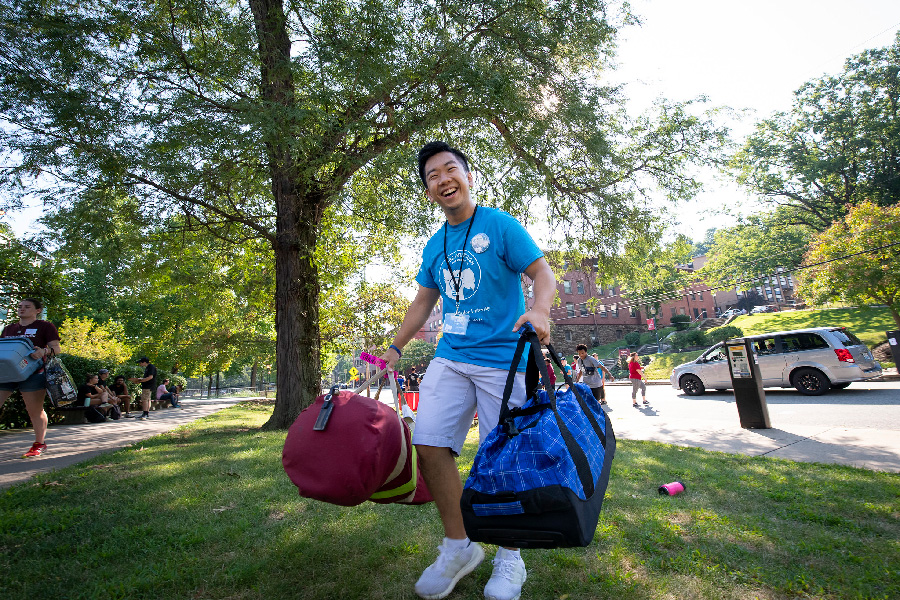 Student in blue shirt carrying two bags during residence hall move-in day on campus