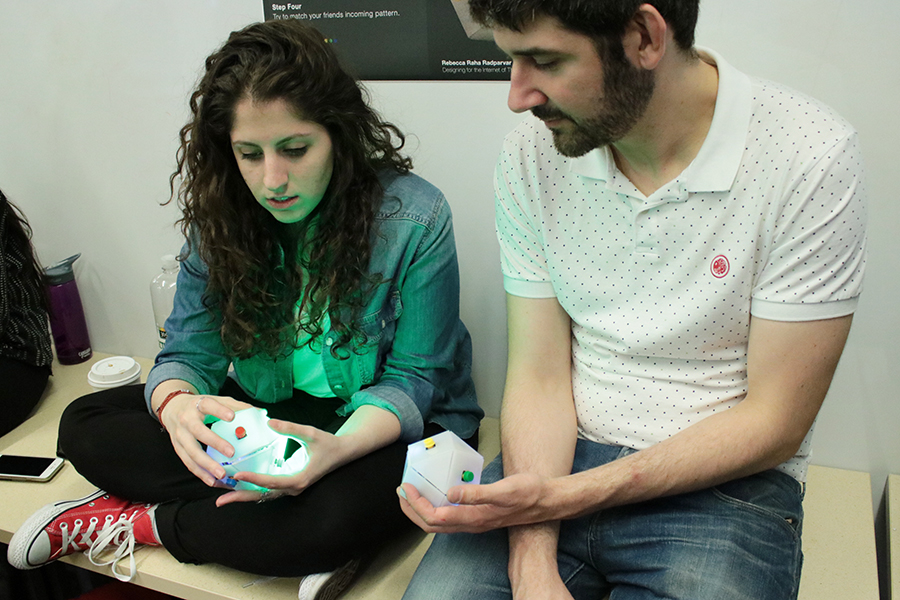 Two people holding Bazi devices. The devices are shaped like balls, with colored buttons around them. One player's Bazi device is lit up.
