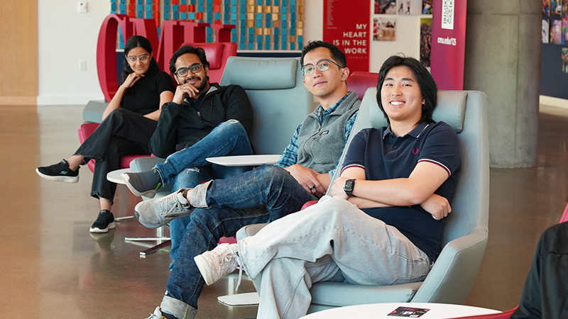 Four students relax together in lounge chairs inside a bright common area