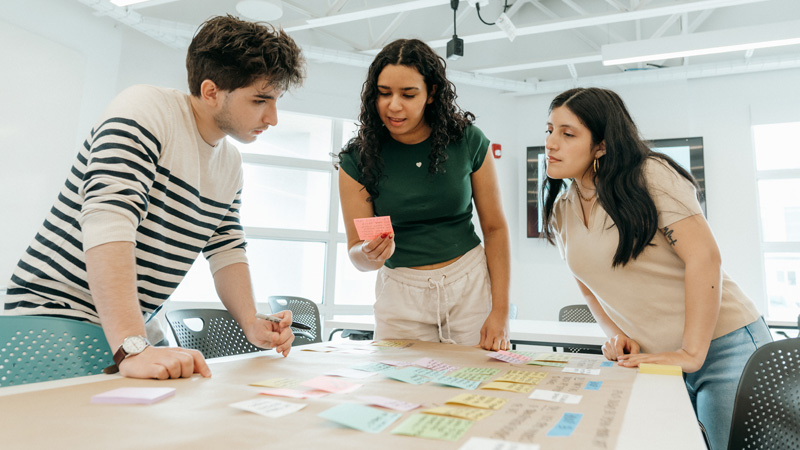 Three students arrange colorful sticky notes across a table during a brainstorming session