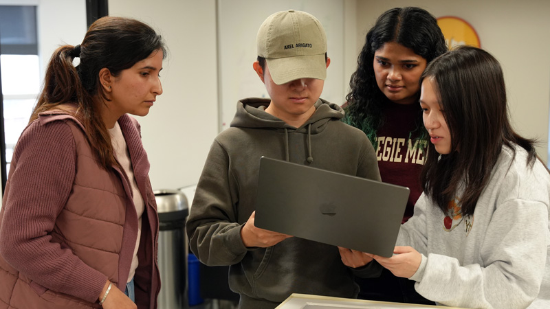 Four students gather around a laptop to review something together