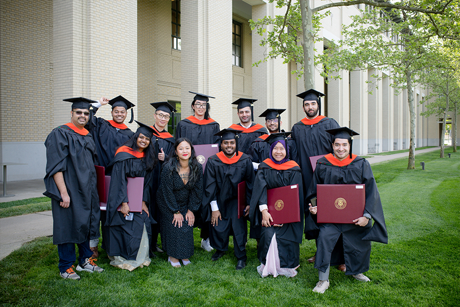 A group of students poses in front of a building wearing their graduation attire