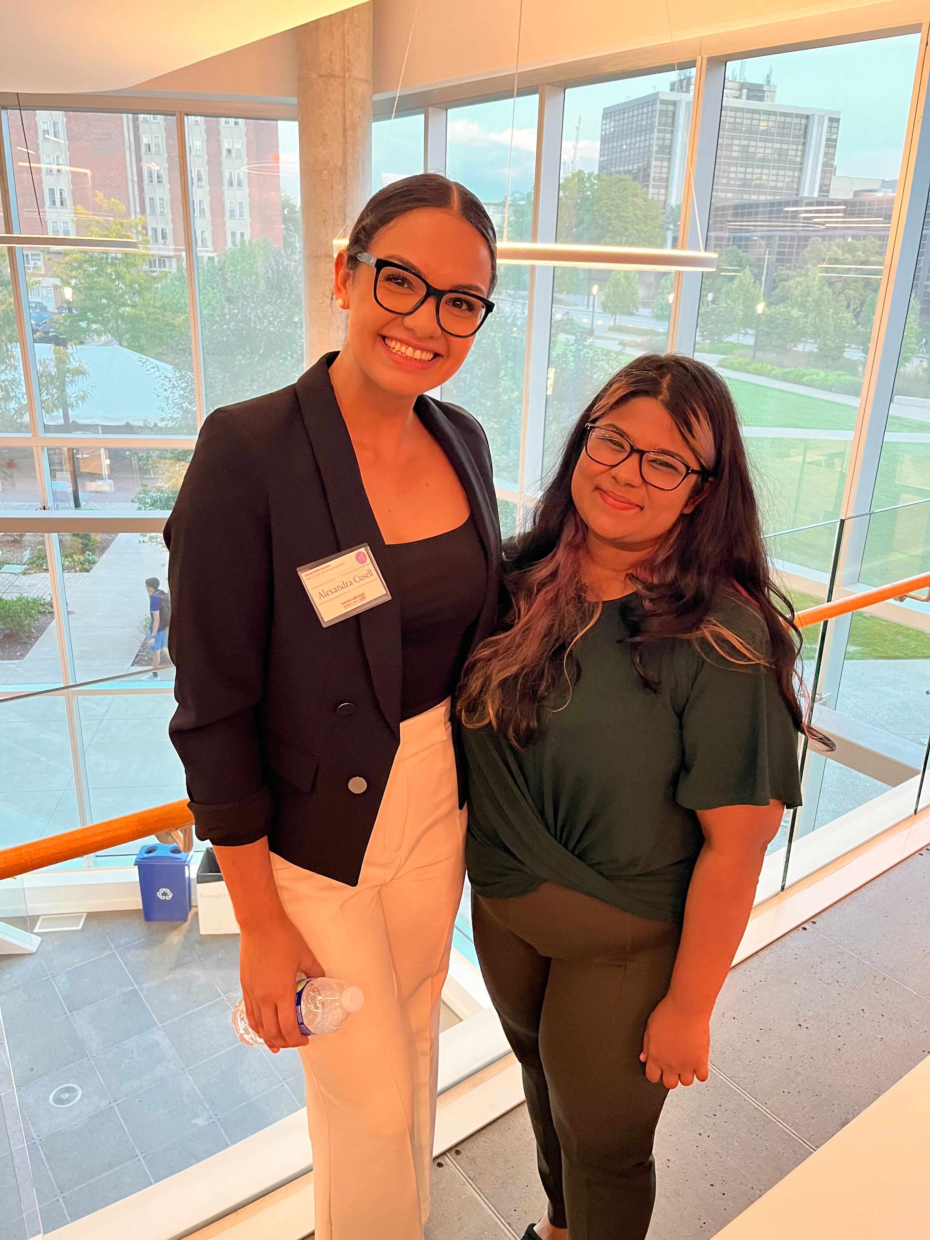 Alex poses with another iii student in the Tepper Building on campus. The pair are in front of a large set of windows.