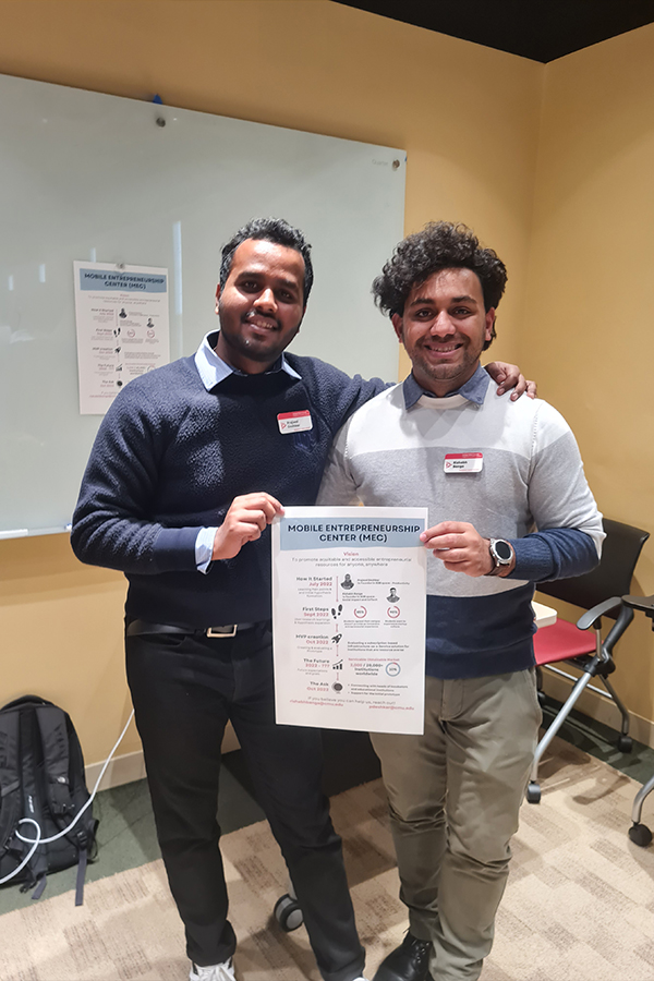 Prajwal and Rishabh pose together holding a slide from their startup presentation