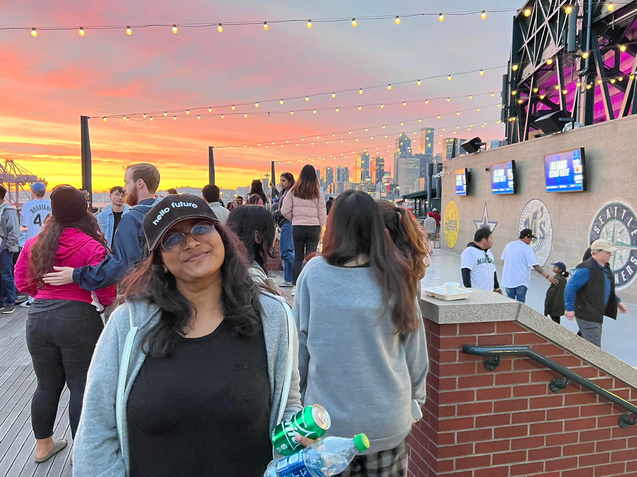 student pranathi alla stands on a rooftop on a summer evening. behind her, the sky is bright orange and red with the setting sun.