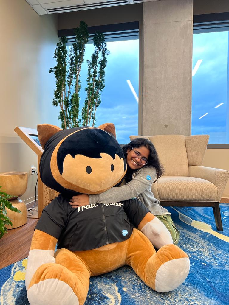 student pranathi alla is hugging a large stuffed mascot from her internship company, Salesforce, in a lounge room at the company