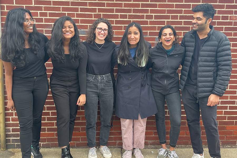 A group of students stands in front of a brick wall, they are laughing and smiling