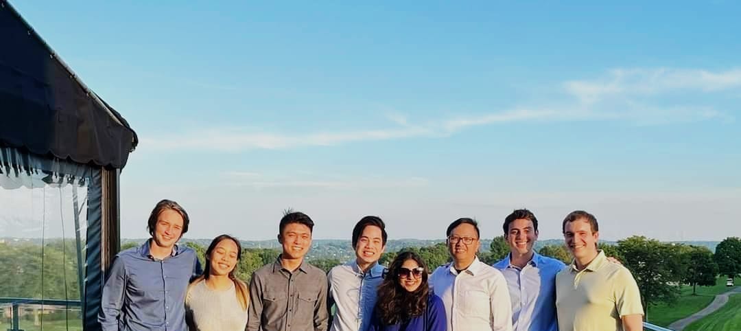 student trishala pillai and fellow interns take a photograph in front of a vast green landscape. the sky is a tinted blue color and the sun is setting behind them