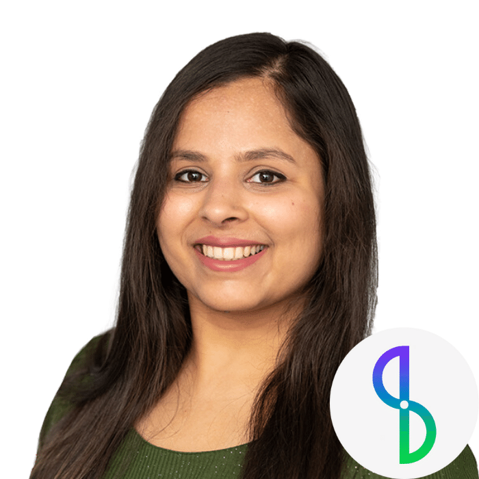 Agarwal has brown wavy hair past her shoulders. She is wearing a long-sleeved olive green top. Located in the lower right corner, the company's logo merges S and B into one image, in a gradient from blue to purple to green.