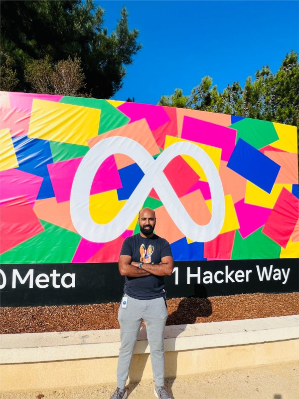With his arms crossed, Rasool poses in front of Meta's sign on a blue-sky day at 1 Hacker Way
