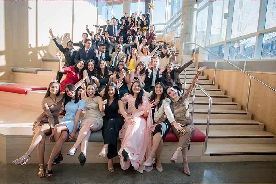 A group of about 40 students sit on a set of stairs.Their arms are extended and waving and they are smiling and cheering with excitement and joy