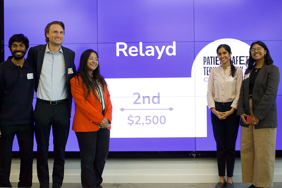 A group of students poses for a photo in front of a digital screen that reads "Relayd"