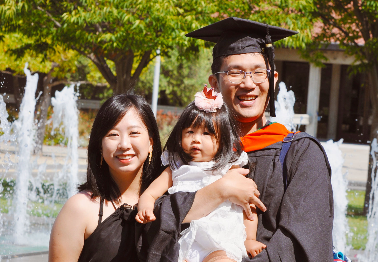 couple holding a child. the man is wearing a graduation gown