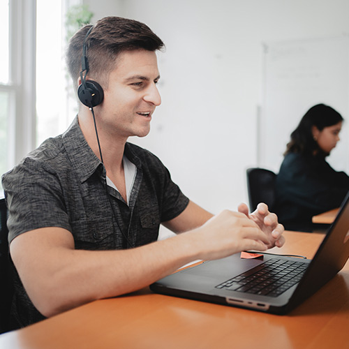 male student is engaged in an online course and talking with his peers over a headset