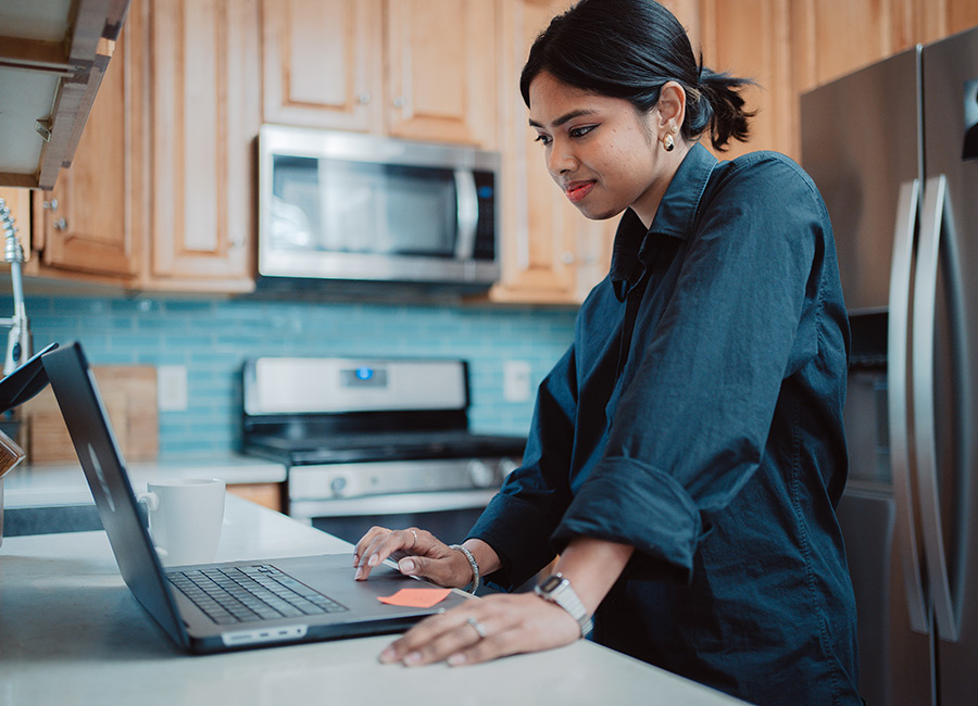 a female online student is working on a project in her kitchen on her laptop computer