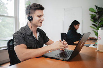 male working at a laptop computer while talking into a headset