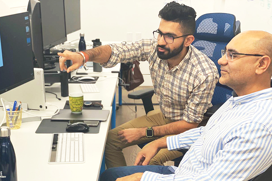 Manish Chhabra at a desk talking with colleague