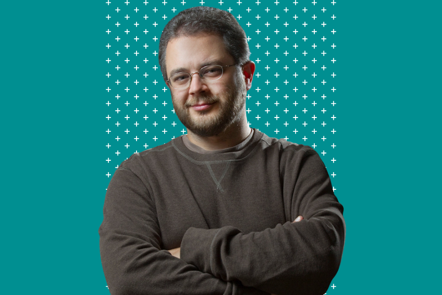 A picture of Patrick Tague on a teal background with a repeating "+" design