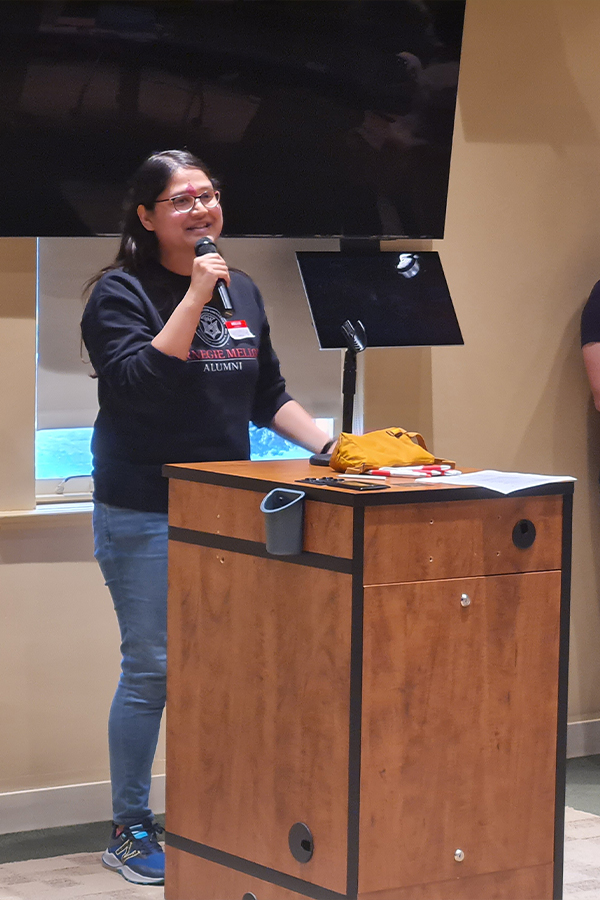 Shivani is standing at a podium holding a microphone while presenting her startup pitch