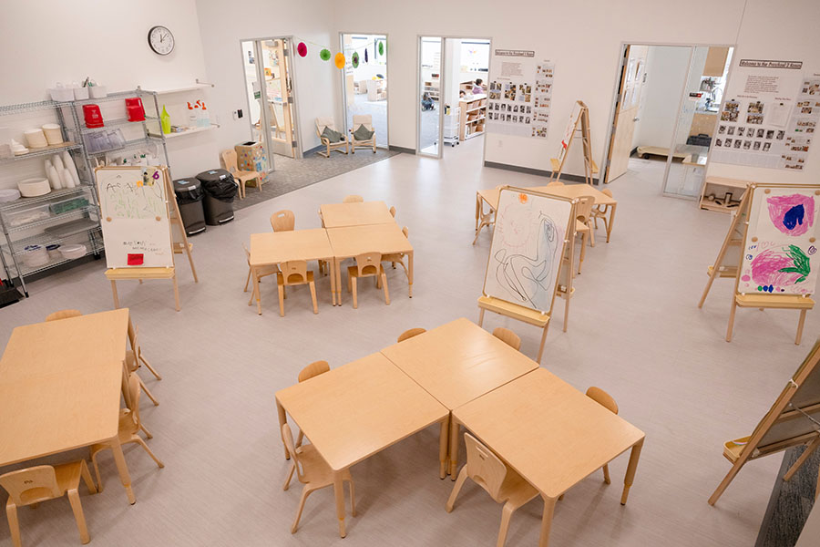 Cyert Center preschool classroom showing a bright, tidy space with child-sized tables and chairs, easels with children's drawings, and shelves of art supplies 