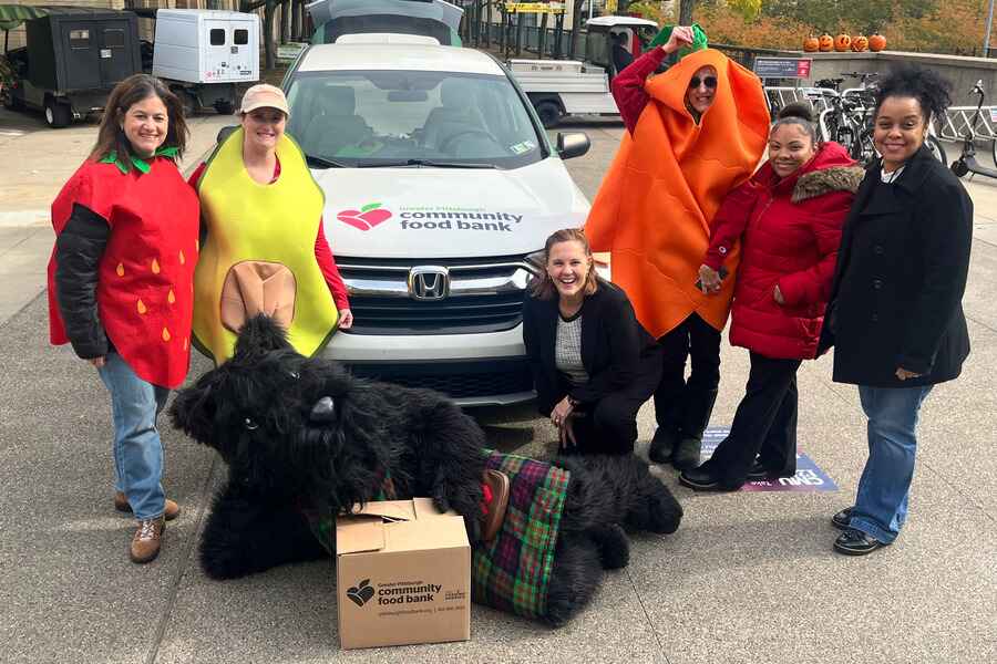 Staff Council Food Drive Committee posing with Scotty Dog mascot in front of Greater Pittsburgh Community Food Bank car and wearing different food costumes
