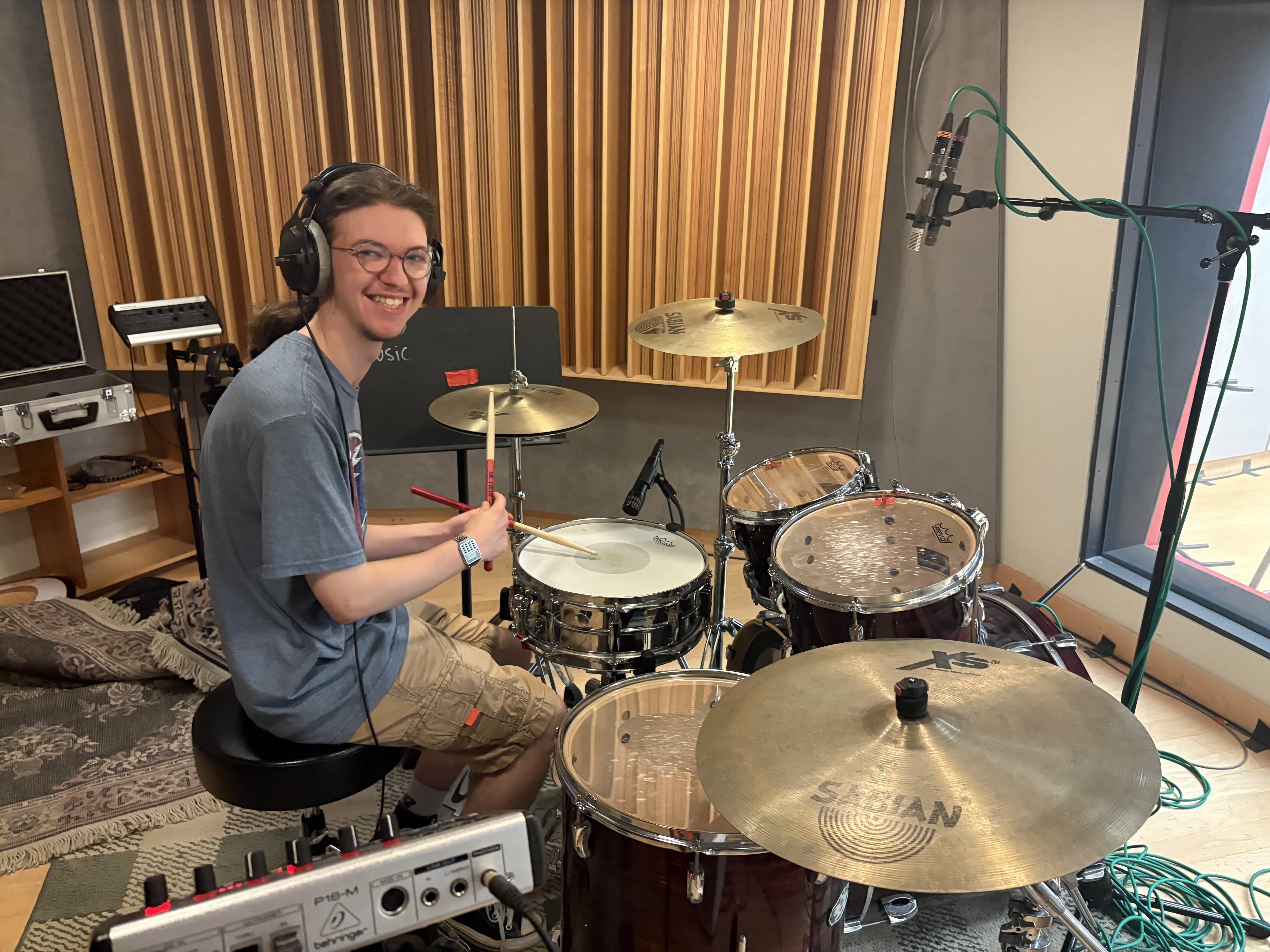 Student smiling while sitting at a full drum kit with headphones on.
