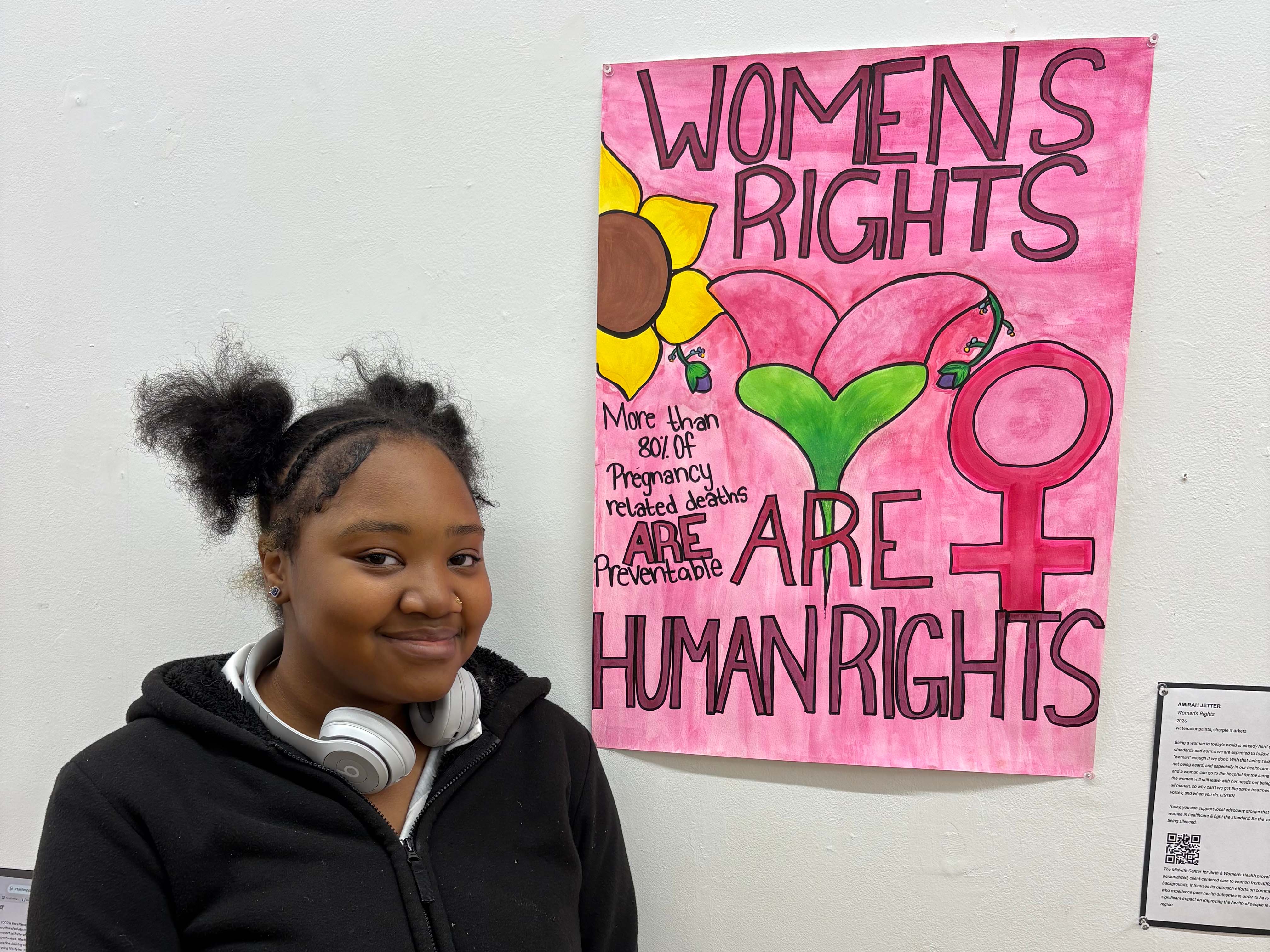 Student standing in front of a painting displaying the words "Women's rights are human rights."