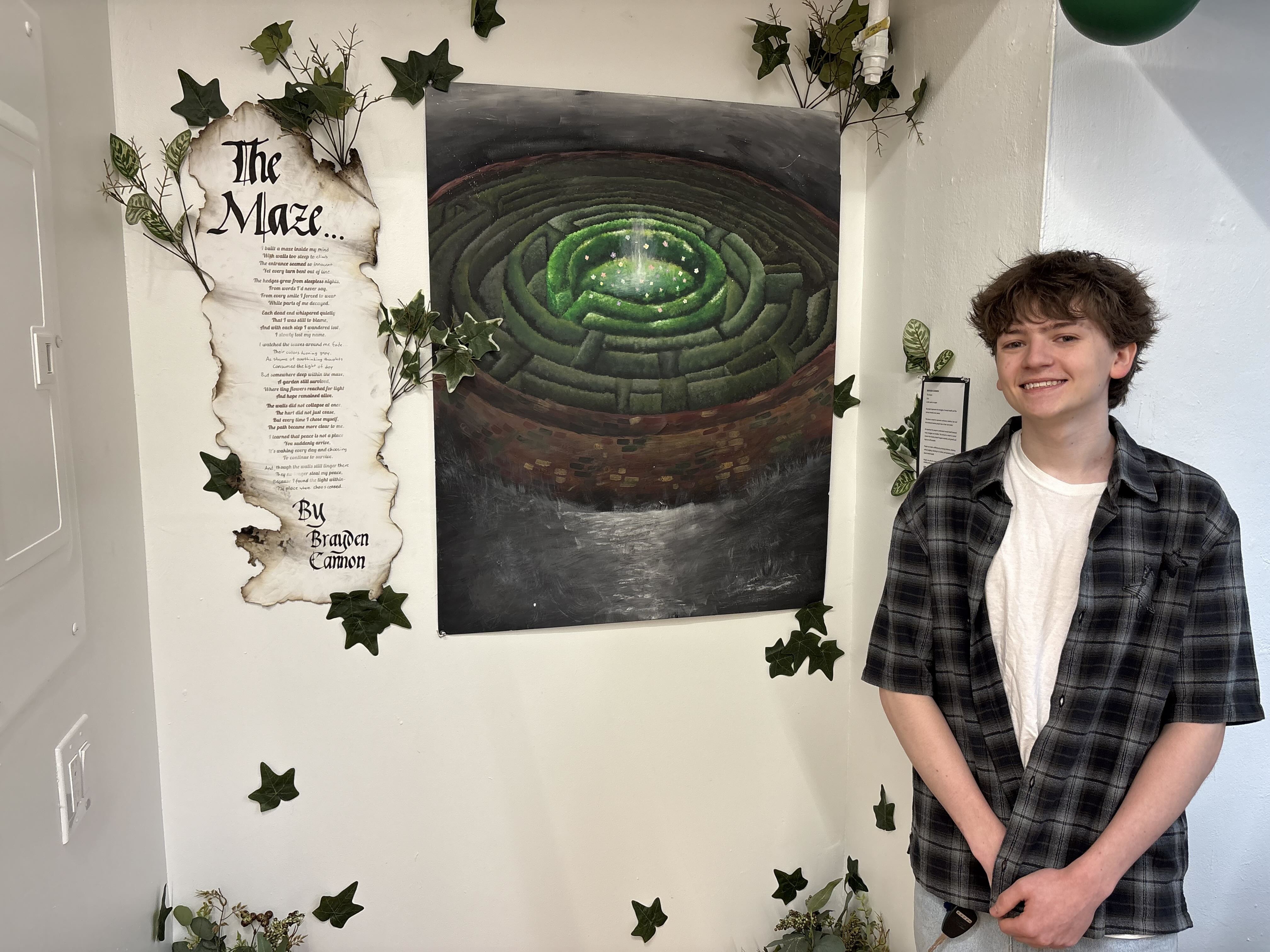 Student standing next to a painting of a maze next to a poem written on aged paper, surrounded by ivy vines.