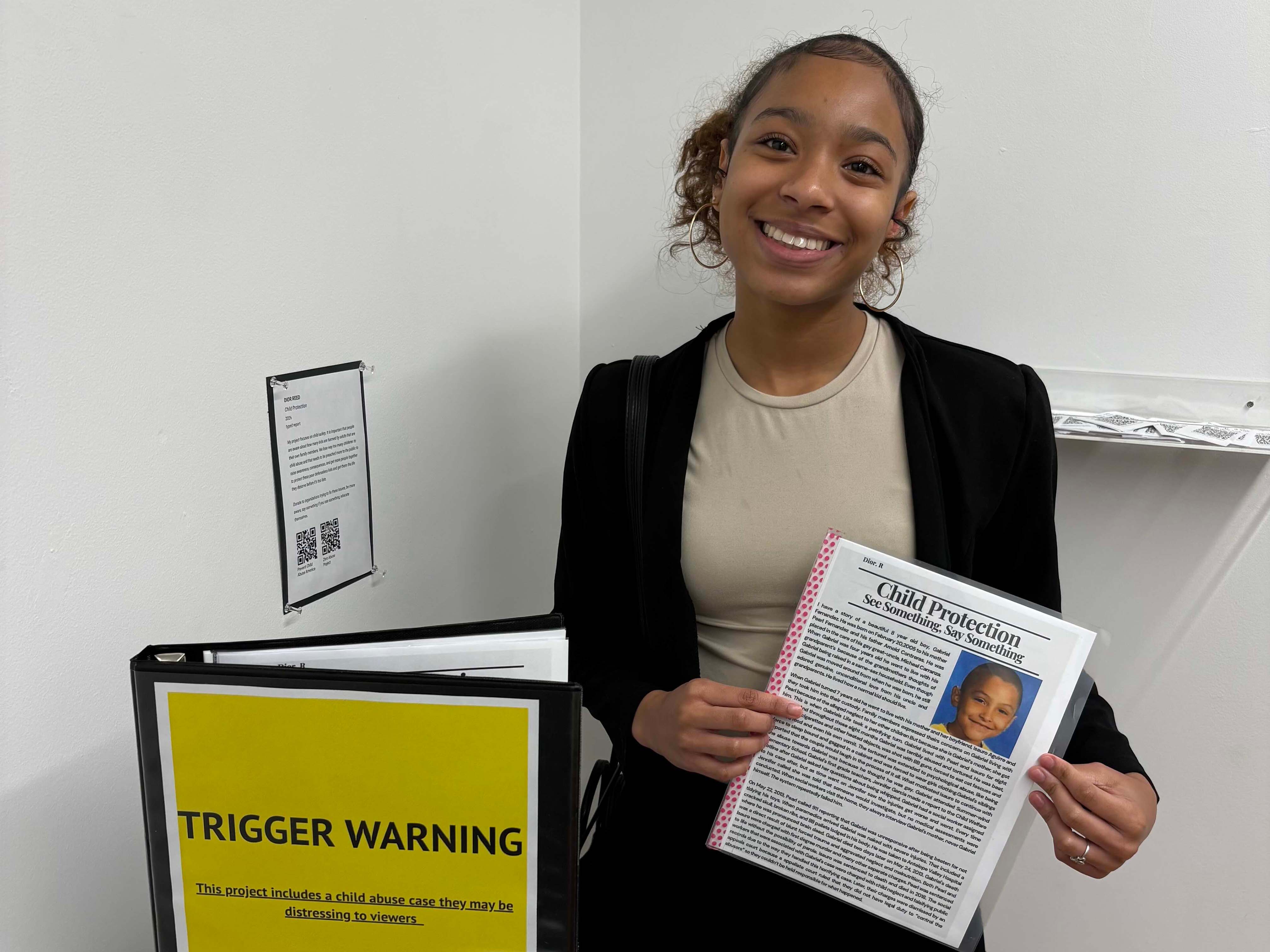 Standing smiling and holding a paper report next to a bright yellow binder.