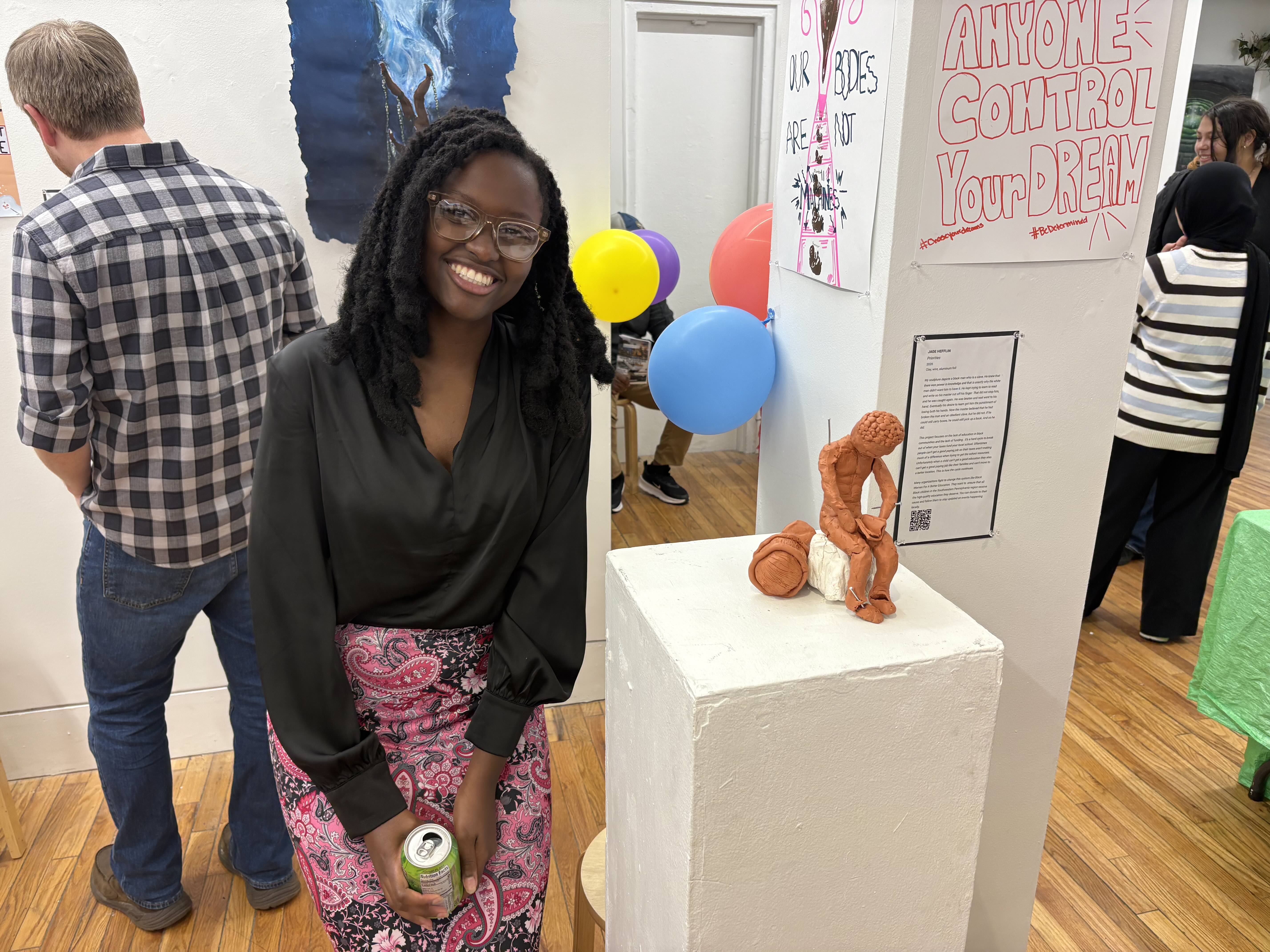Student smiling standing next to a clay sculpture on a pedestal. 