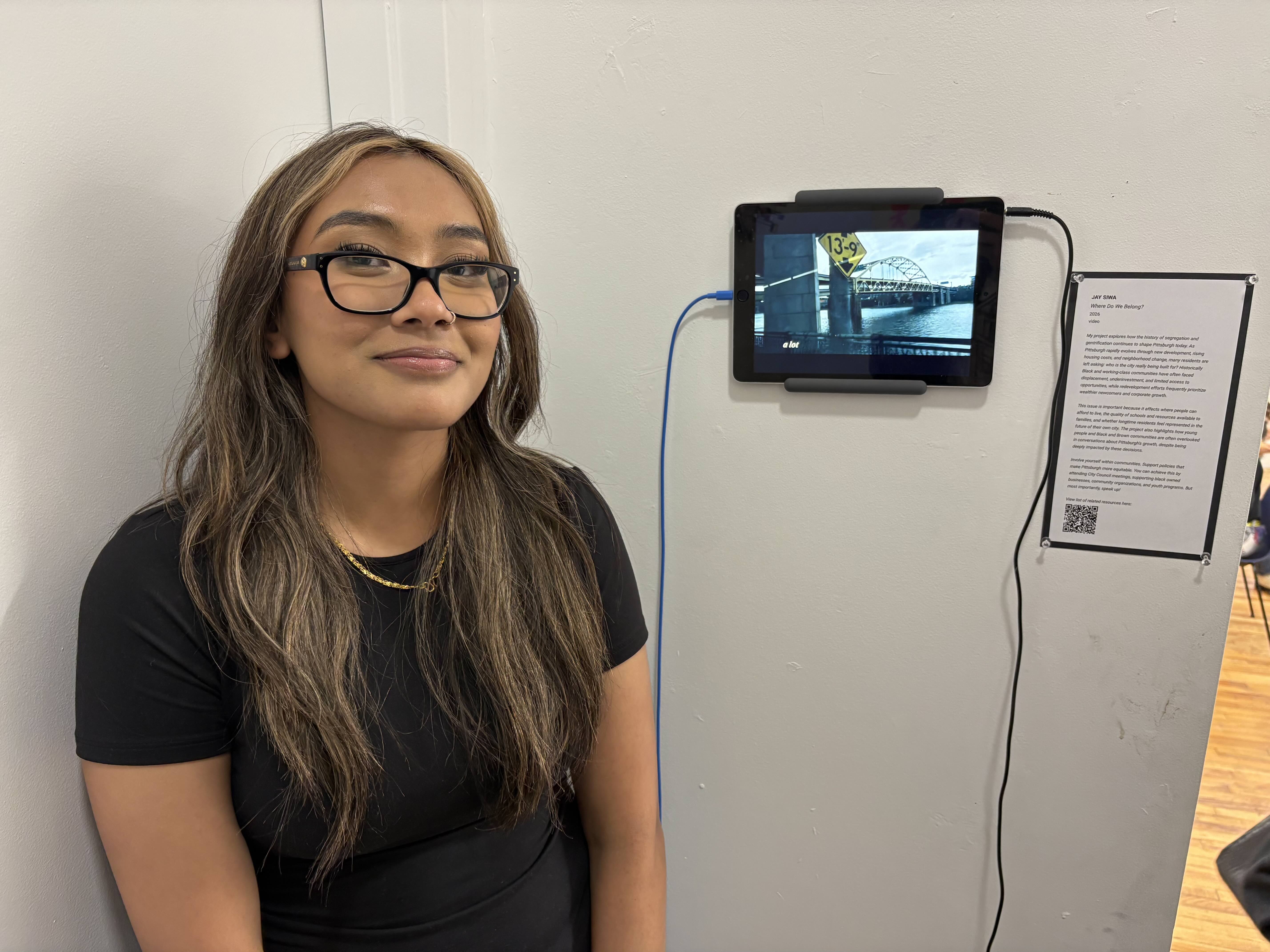 Student standing next to a wall-mounted iPad playing a video.