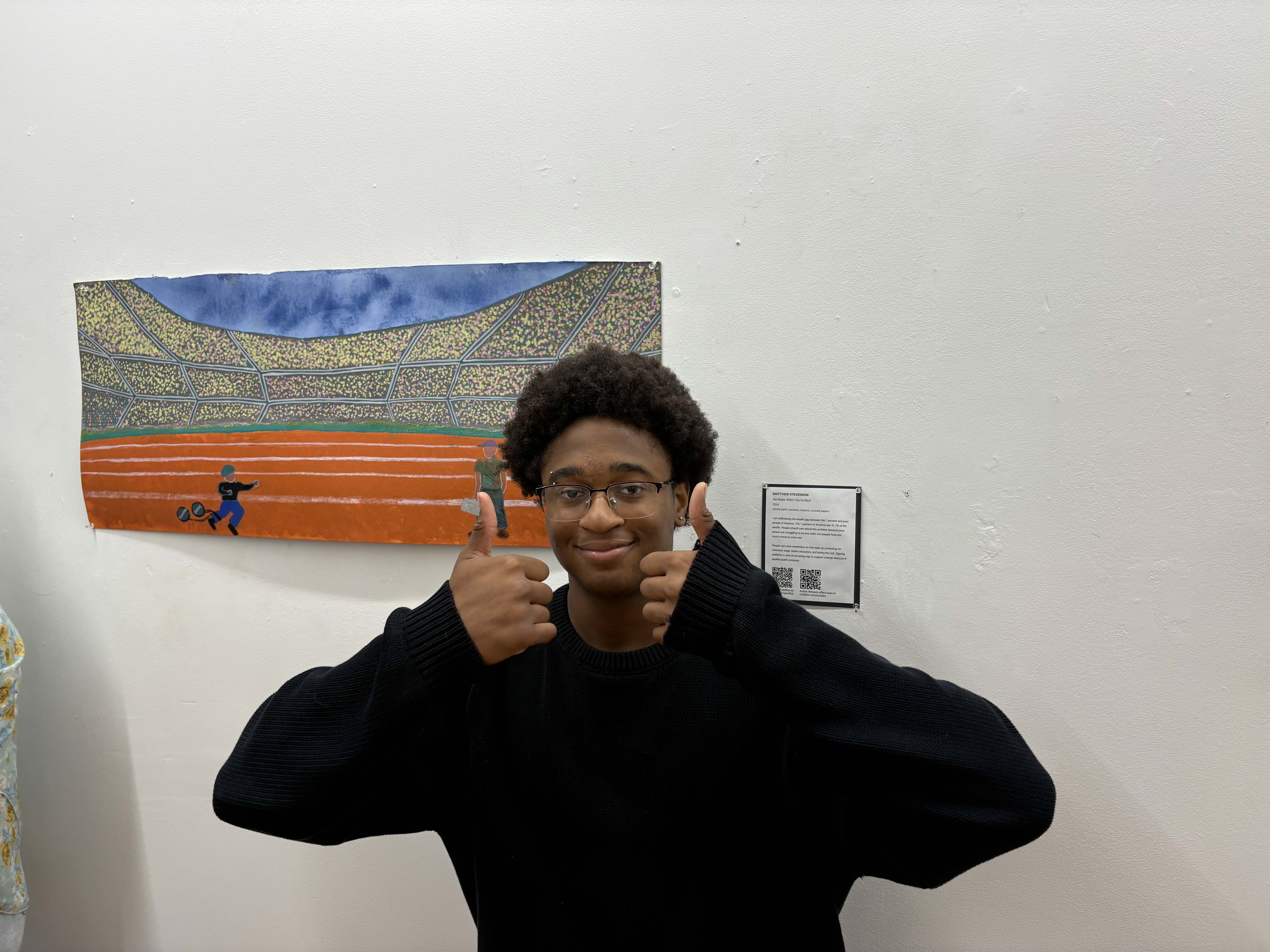 Student giving thumbs up next to a horizontal painting of a stadium.