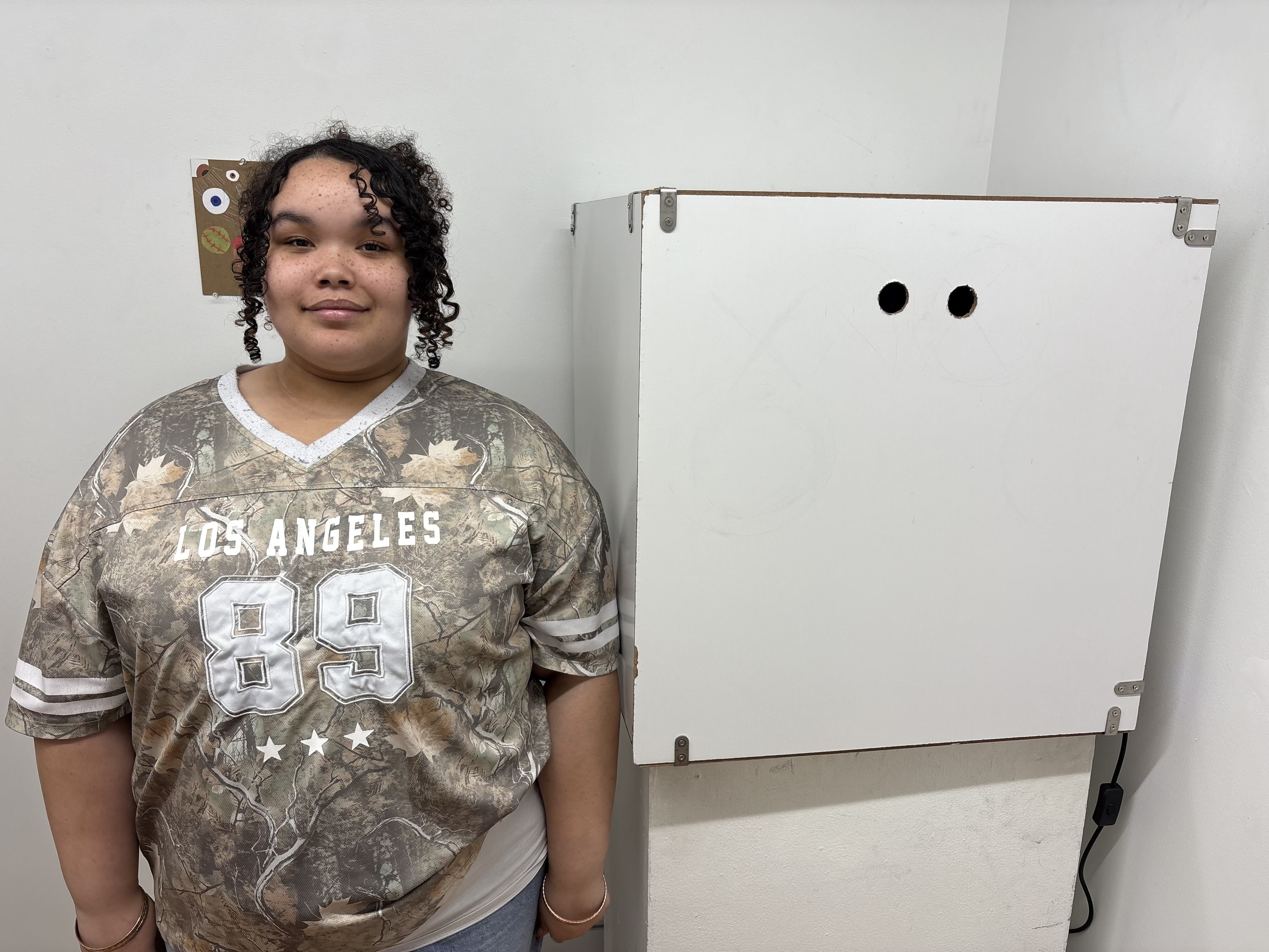 Student standing next to white box with holes cut out for people to look through.
