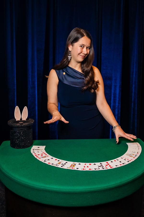 Young female standing at a green table with  playing cards spread on it.