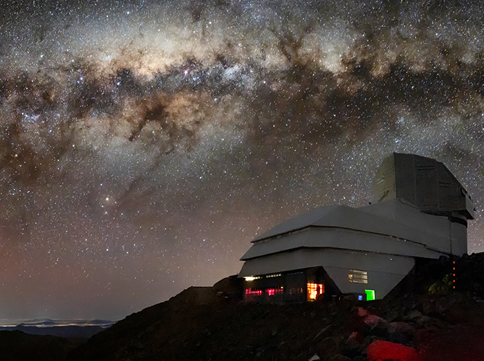 An observatory sits on a mountain underneath a glittering view of the Milky Way
