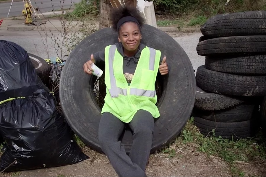 photo of volunteer playfully giving two thumbs up while sitting in an abandoned tire