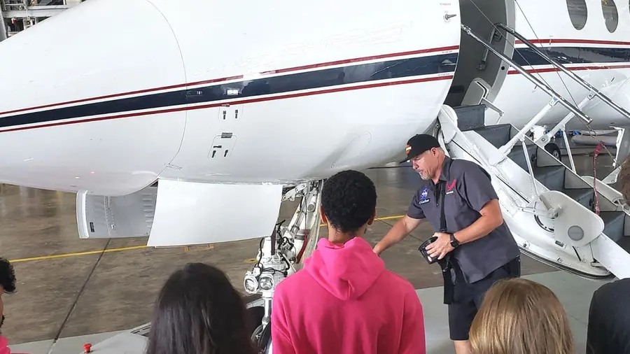 People standing in front of an airplane in a hangar on the ground.