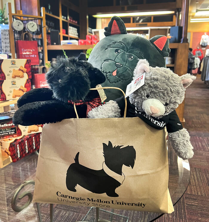 A paper bag with a CMU Scotty dog printed on it is full of stuffed animals on a display at the Bookstore.