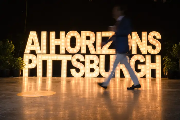 Someone walks by a large sign of the letters "AI Horizons Pittsburgh" spelled out by lightbulbs.