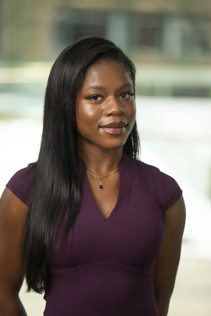 A waist-up photo of a woman with long black hair in a purple shirt looking straight at the camera.