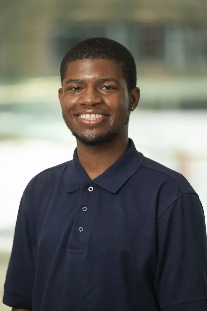 A man with short hair wearing a dark blue shirt smiles for a waist-up portrait